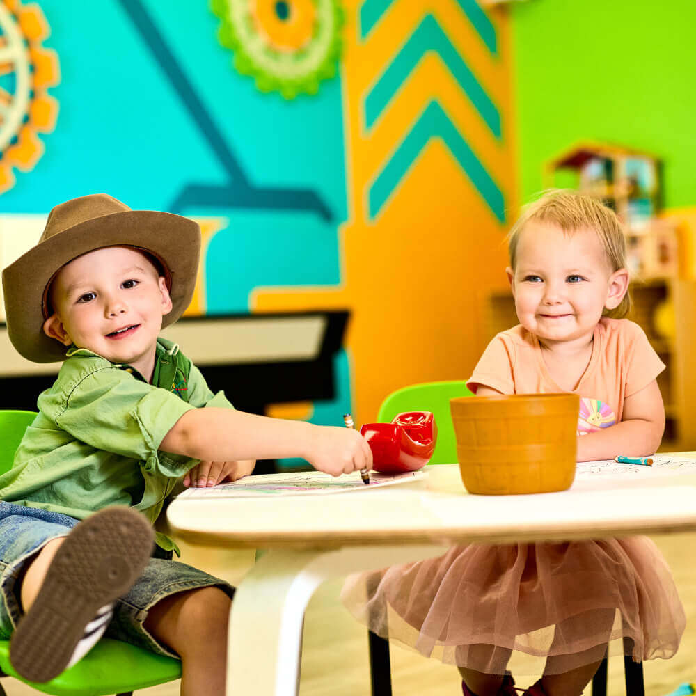 Children enjoy playtime at a colorful Village Clubs Camelback playroom, exploring toys together at a small table.