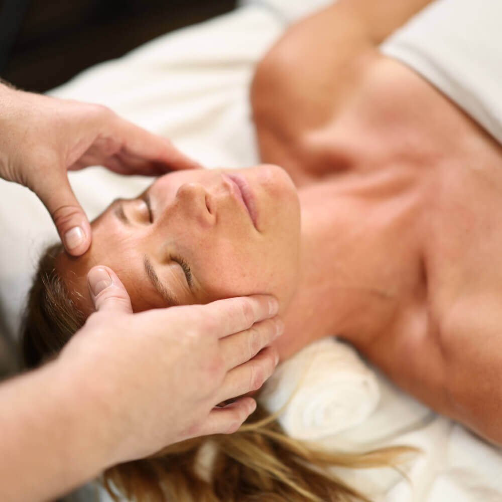 A woman enjoys a relaxing face massage at Village Clubs Camelback, eyes closed as a therapist gently massages her face.