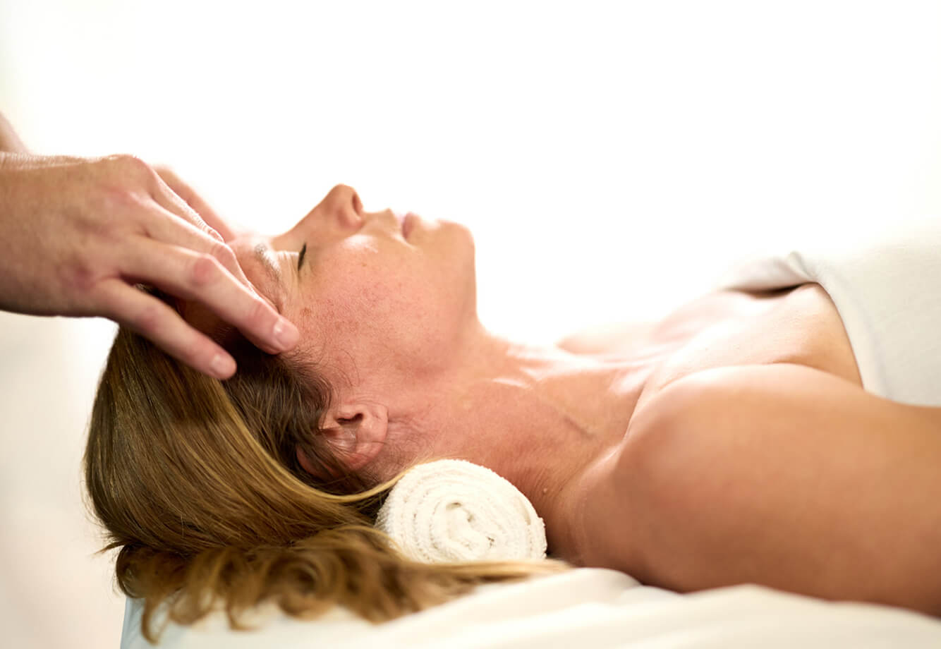 A woman enjoys a relaxing head massage at Village Clubs Camelback, eyes closed and wrapped in a towel for spa comfort.