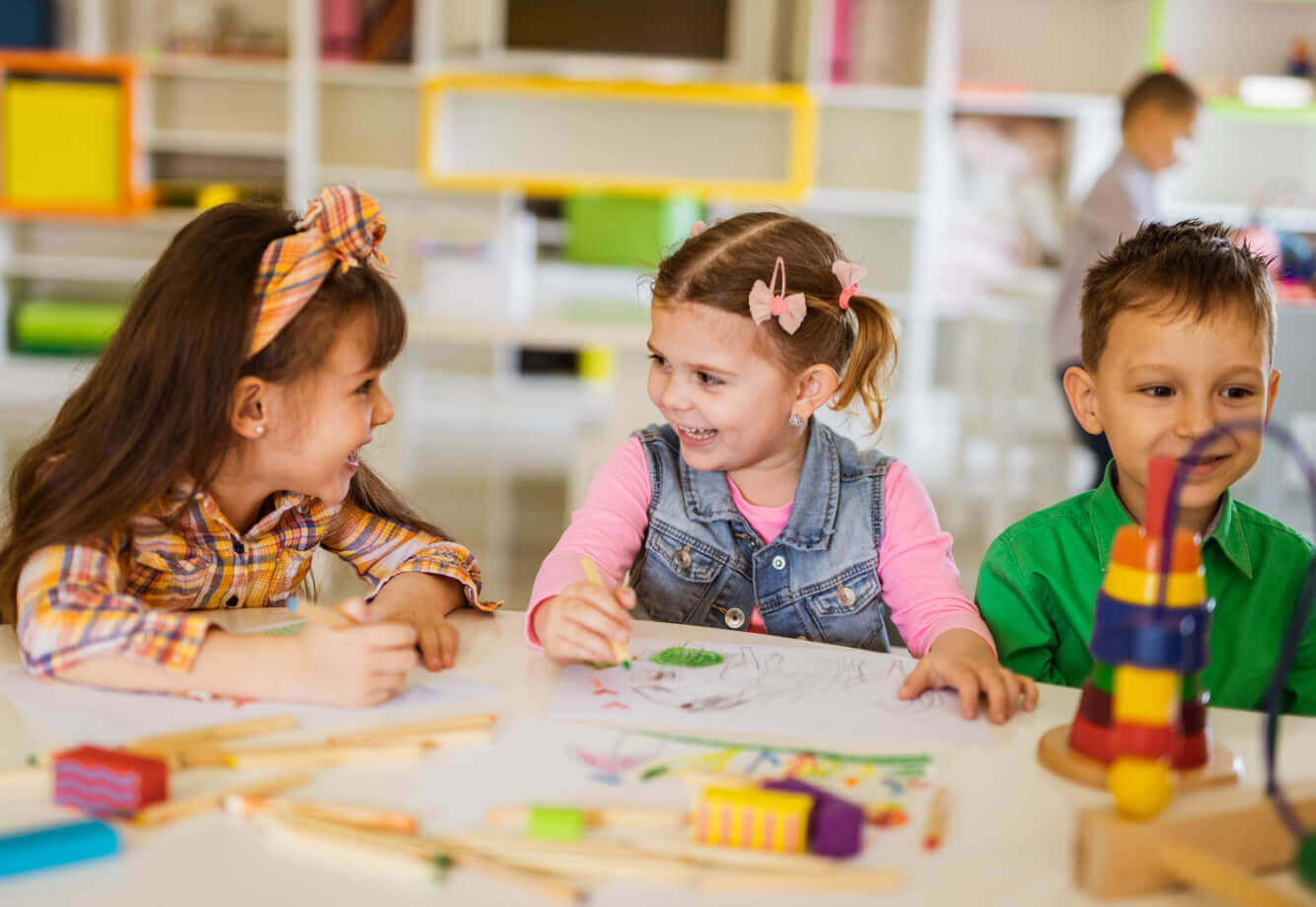 Children drawing and coloring together at Village Clubs Camelback, surrounded by art supplies and toys in a bright activity room.