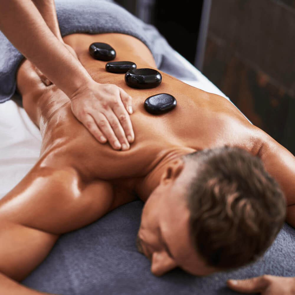 At Village Clubs Camelback, a man enjoys a hot stone massage on a spa table in a serene, professional setting.