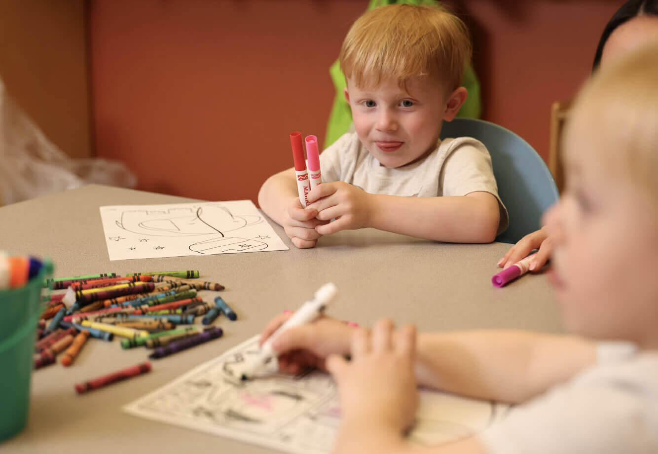 Children color with markers and crayons at Village Clubs Camelback, enjoying creative activities at the kids’ facility table.