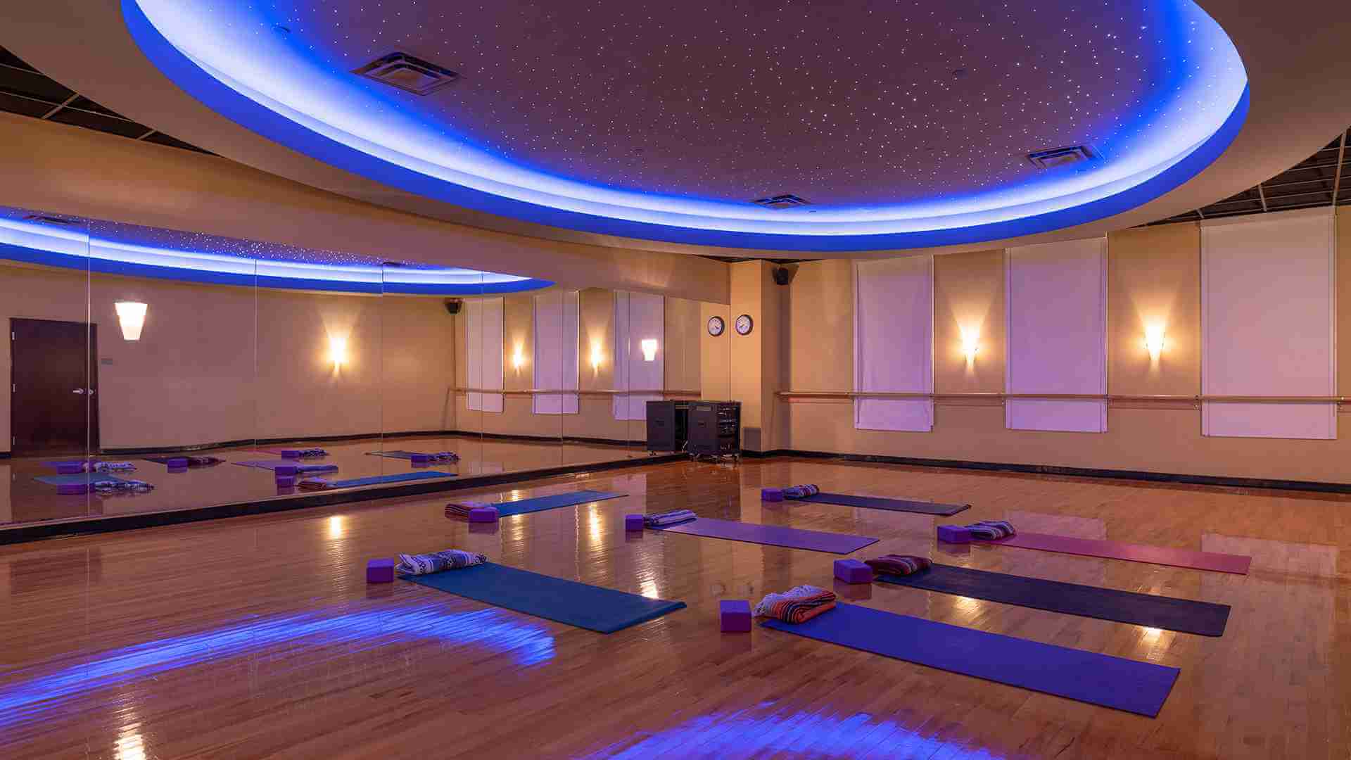Village Clubs DC Ranch yoga studio with wooden floors, arranged mats, large mirrors, soft lighting, and a blue starry ceiling.