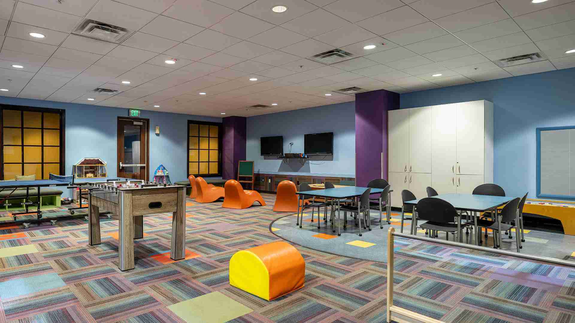 Village Clubs DC Ranch playroom with bold carpet, foosball, TVs, bright colors, and modern lighting for kids’ activities.