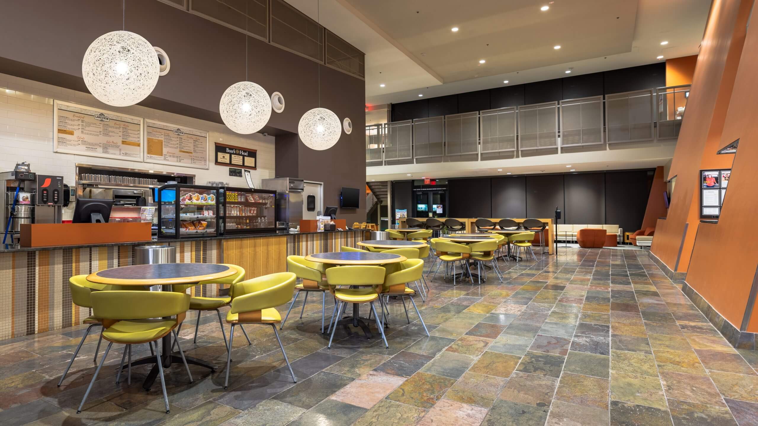 Village Clubs café at Ocotillo features yellow chairs, round tables, warm globe lights, and an inviting counter with menu in Arizona.