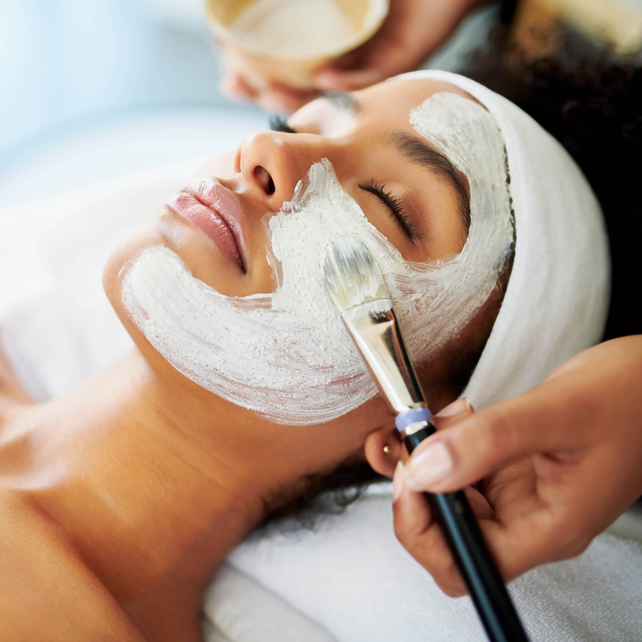 A person receives a facial mask at Village Clubs Camelback, relaxing with eyes closed during a professional spa treatment.