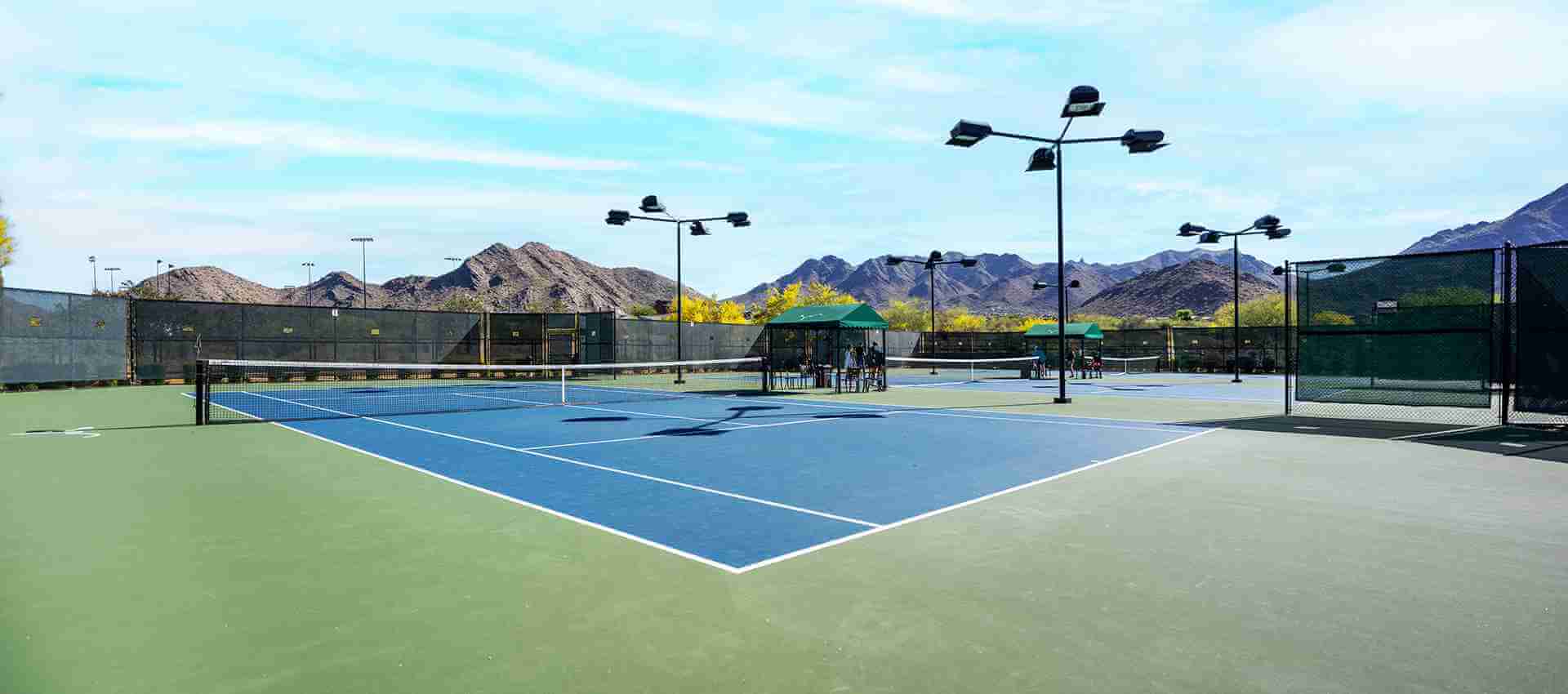 Village Clubs DC Ranch outdoor tennis courts with blue and green surfaces, shaded seating, and scenic mountain views in Arizona.