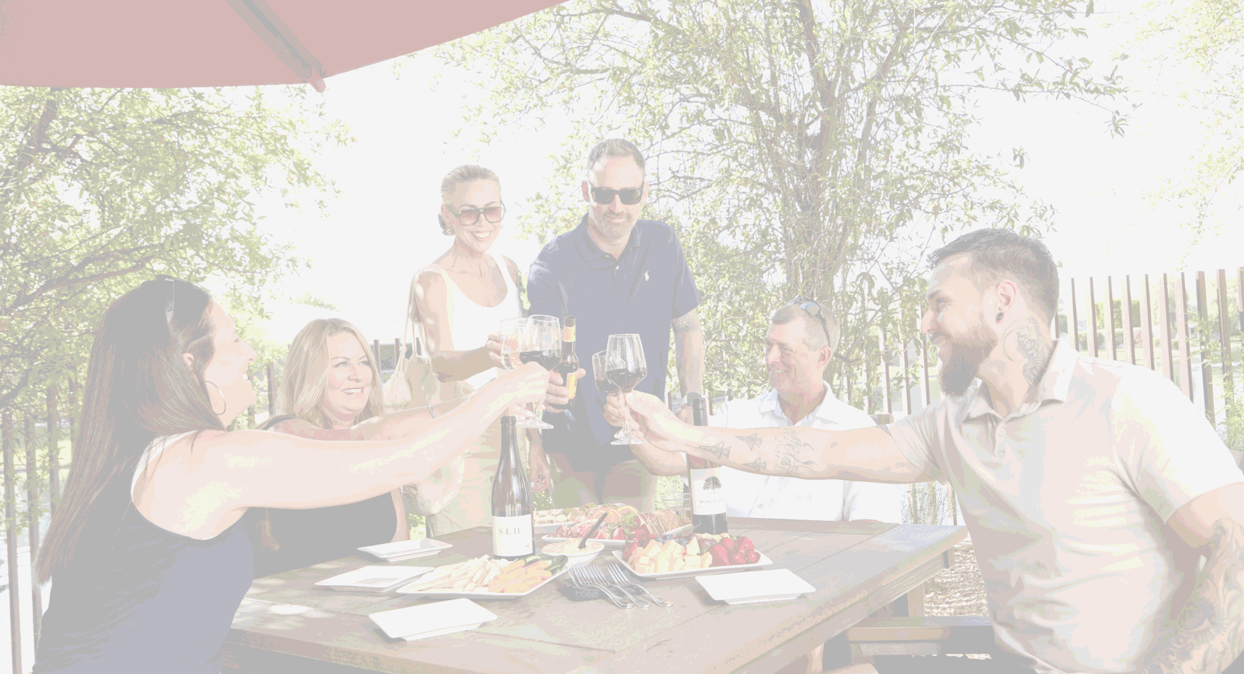 Members toast with wine at a Village Clubs Camelback outdoor table, enjoying snacks under a red umbrella at a community gathering.