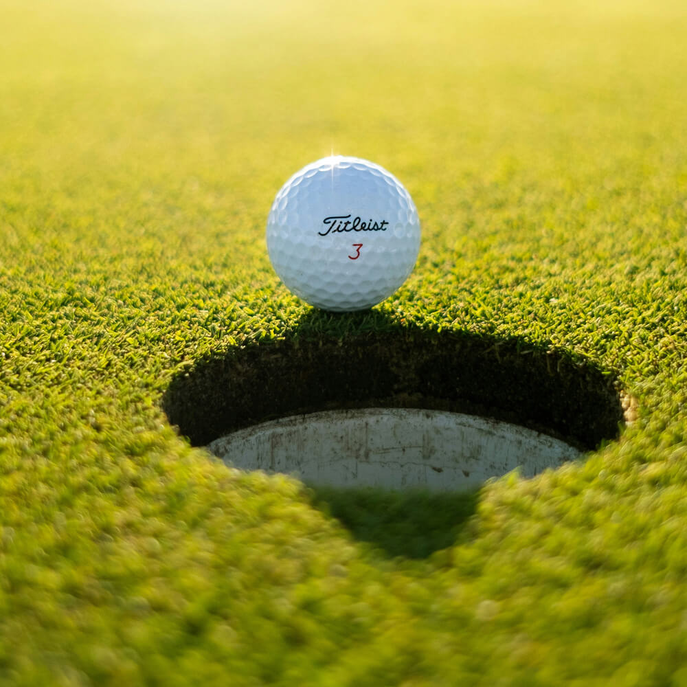 A Village Clubs Titleist golf ball rests near the hole on a sunlit green at Camelback in Arizona, highlighting premier facilities.
