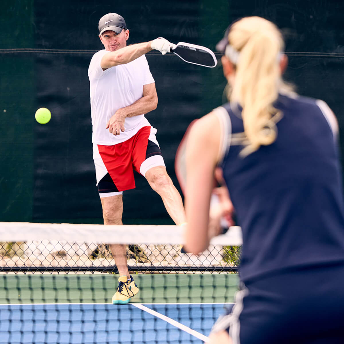 Players enjoy a pickleball match at Village Clubs Camelback in Arizona, with action at the net and both participants ready to compete.