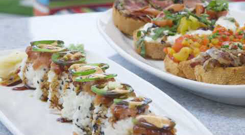 Sushi rolls with jalapeños and sauce at Village Clubs Camelback, with bruschetta and greens in the background.