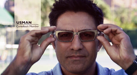 A man adjusts his glasses outdoors at Village Clubs Camelback; text reads 
