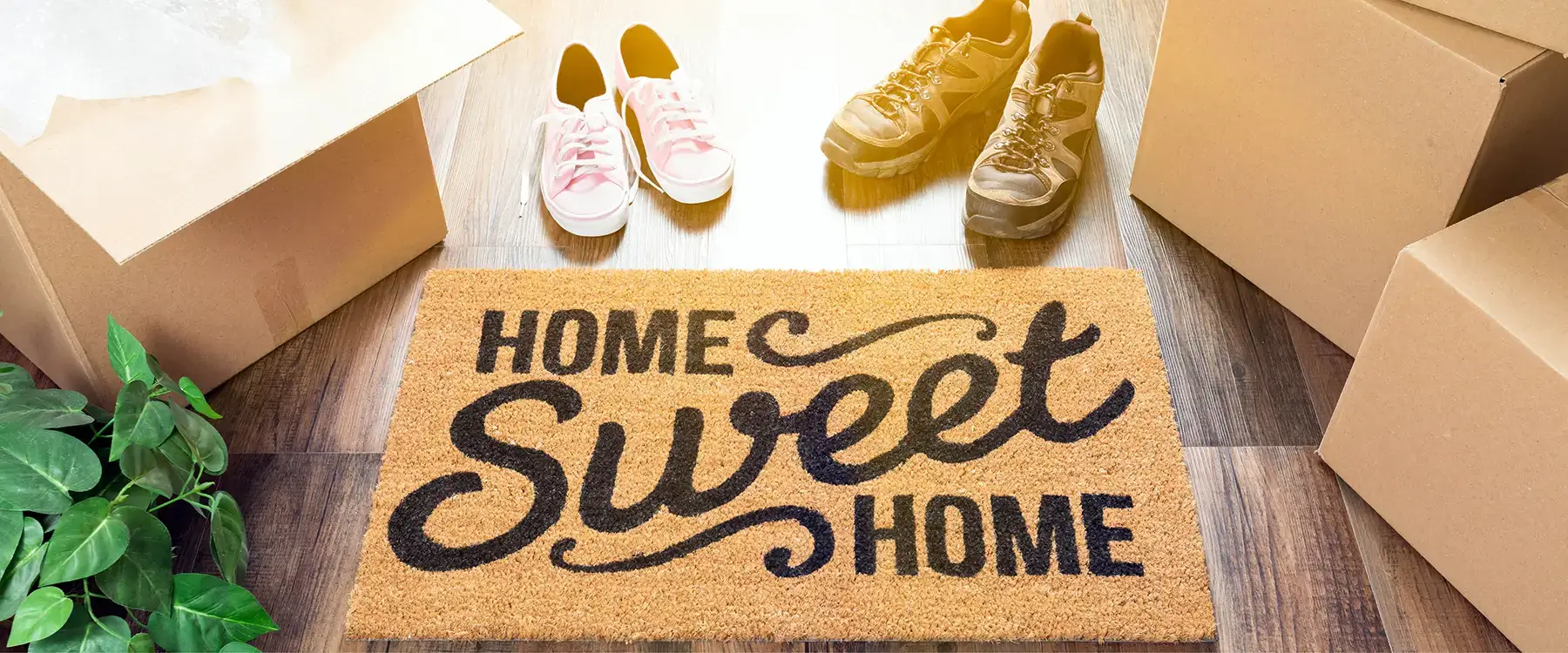 Village Clubs Camelback welcomes new homeowners, with a Home Sweet Home doormat, moving boxes, shoes, and a green plant.