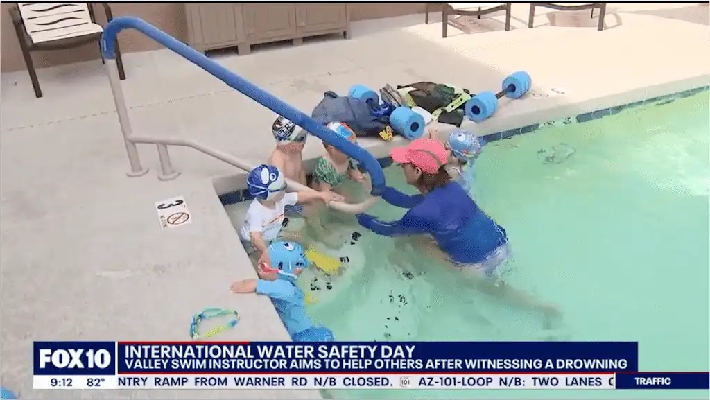 At Village Clubs Camelback, swim instructor guides kids in water safety by the pool, with toys and a FOX 10 banner nearby.