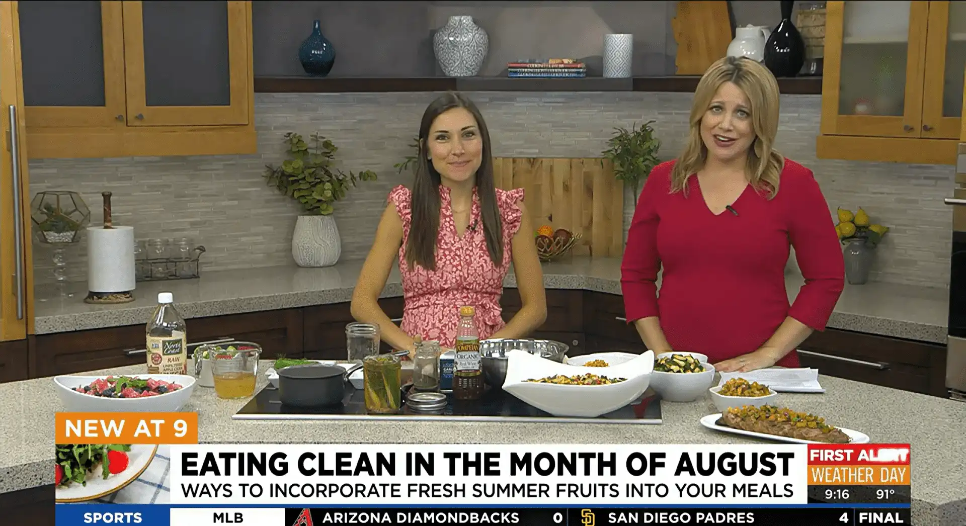 At Village Clubs Camelback, two women share Eating Clean tips in a modern kitchen with fresh dishes and summer fruits.