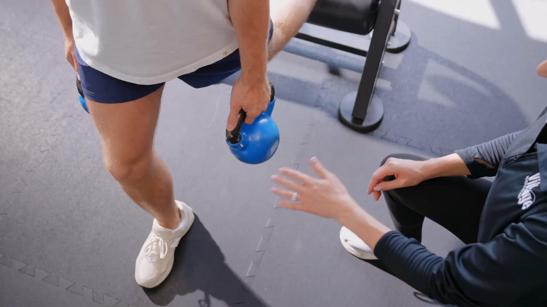 At Village Clubs Camelback gym, a coach assists a member lifting a blue kettlebell during personal training.