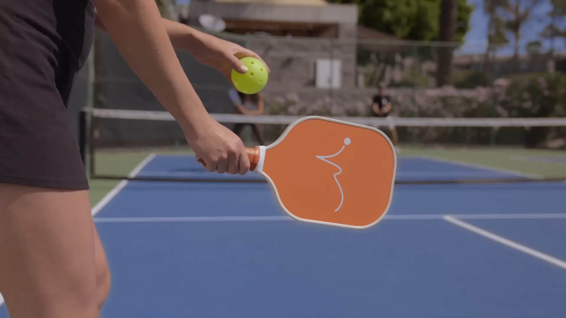 At Village Clubs Camelback in Arizona, a player readies a serve on the blue outdoor pickleball court with paddle and ball in hand.