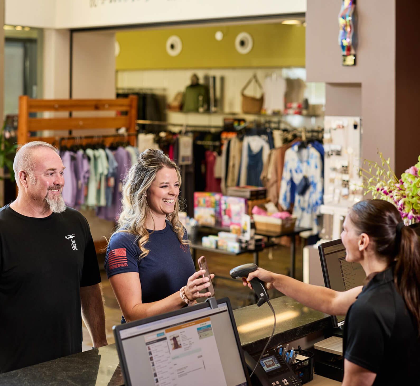 At Village Clubs Camelback, a woman uses her phone to pay at the retail counter as clothing and gifts are displayed behind her.