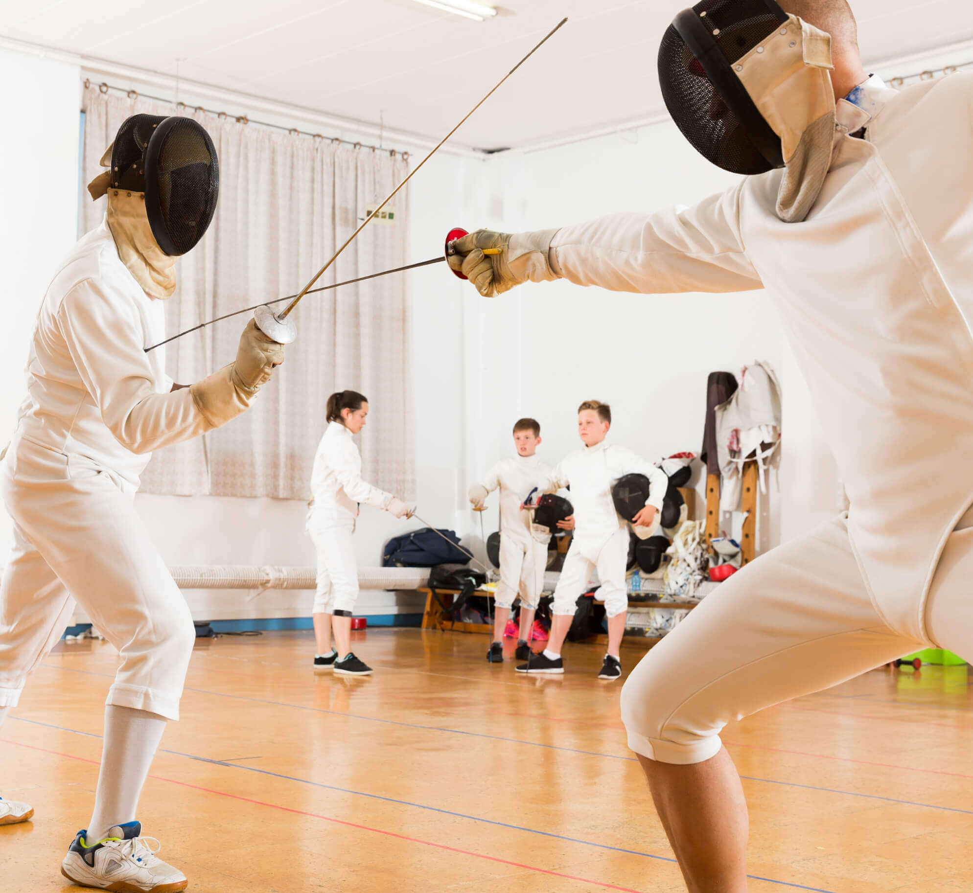 Fencing session at Village Clubs Camelback: two members spar as three others in gear watch and prepare in the gymnasium.