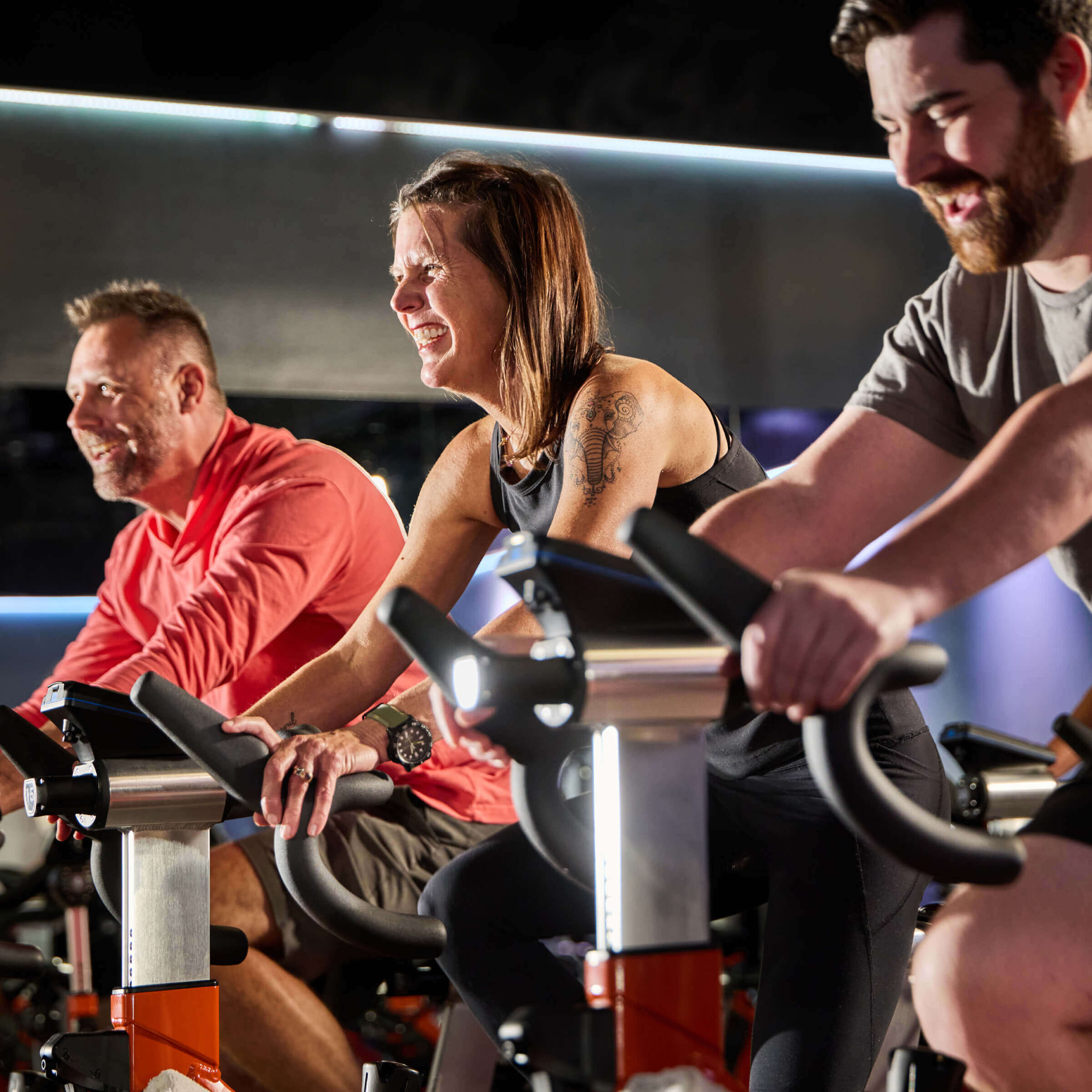 Three people cycle energetically indoors at Village Clubs Camelback, enjoying a lively group workout in bright, modern facilities.