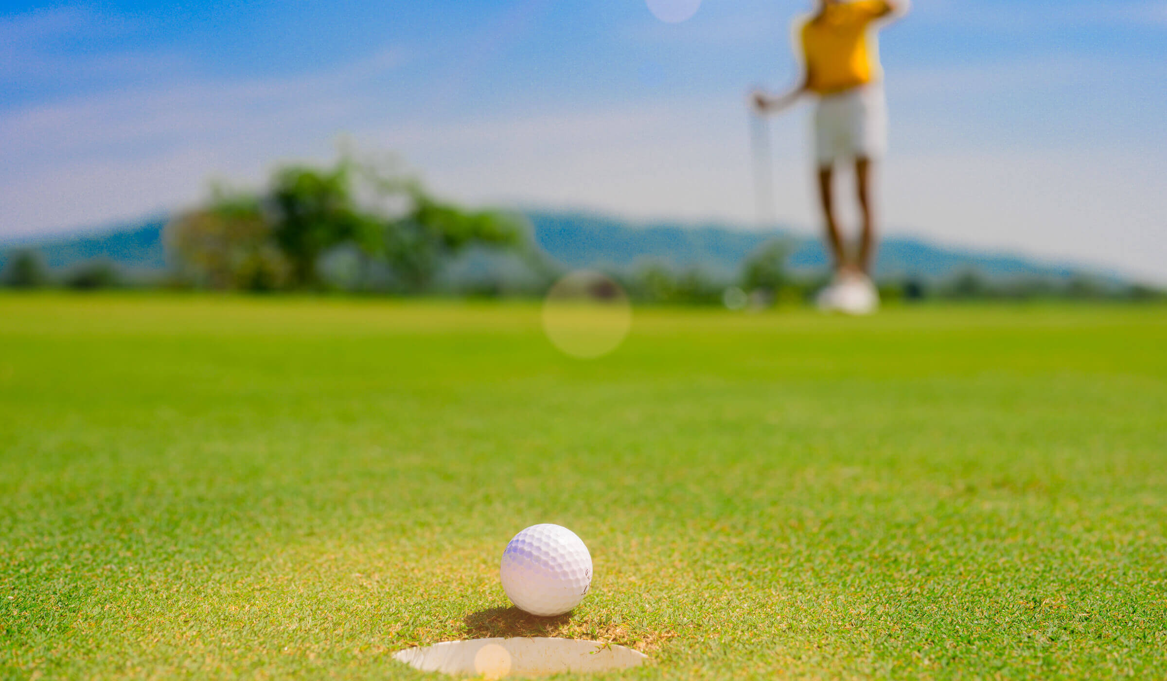 Village Clubs at DC Ranch golf course: close-up of a golf ball near the hole with a golfer in the background on a sunny day.