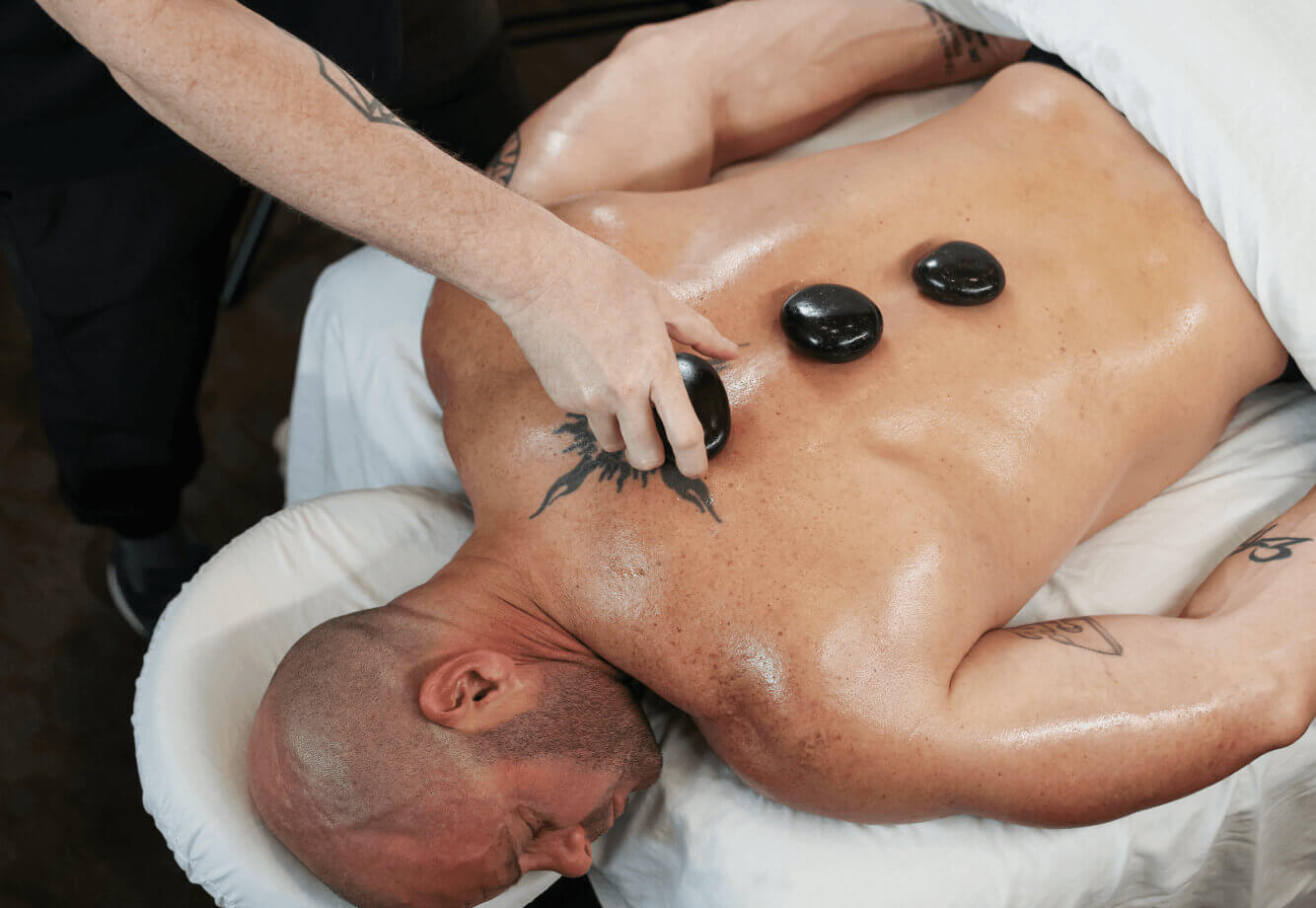 At Village Clubs Camelback, a person enjoys a hot stone massage with smooth stones placed on their oiled back by a therapist.
