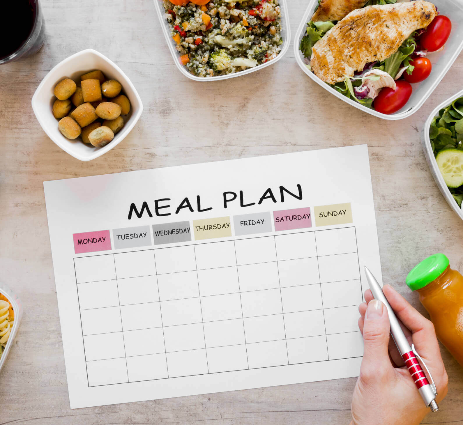 A hand plans meals at Village Clubs Camelback, surrounded by salads, grilled chicken, olives, and juice on a blank sheet.