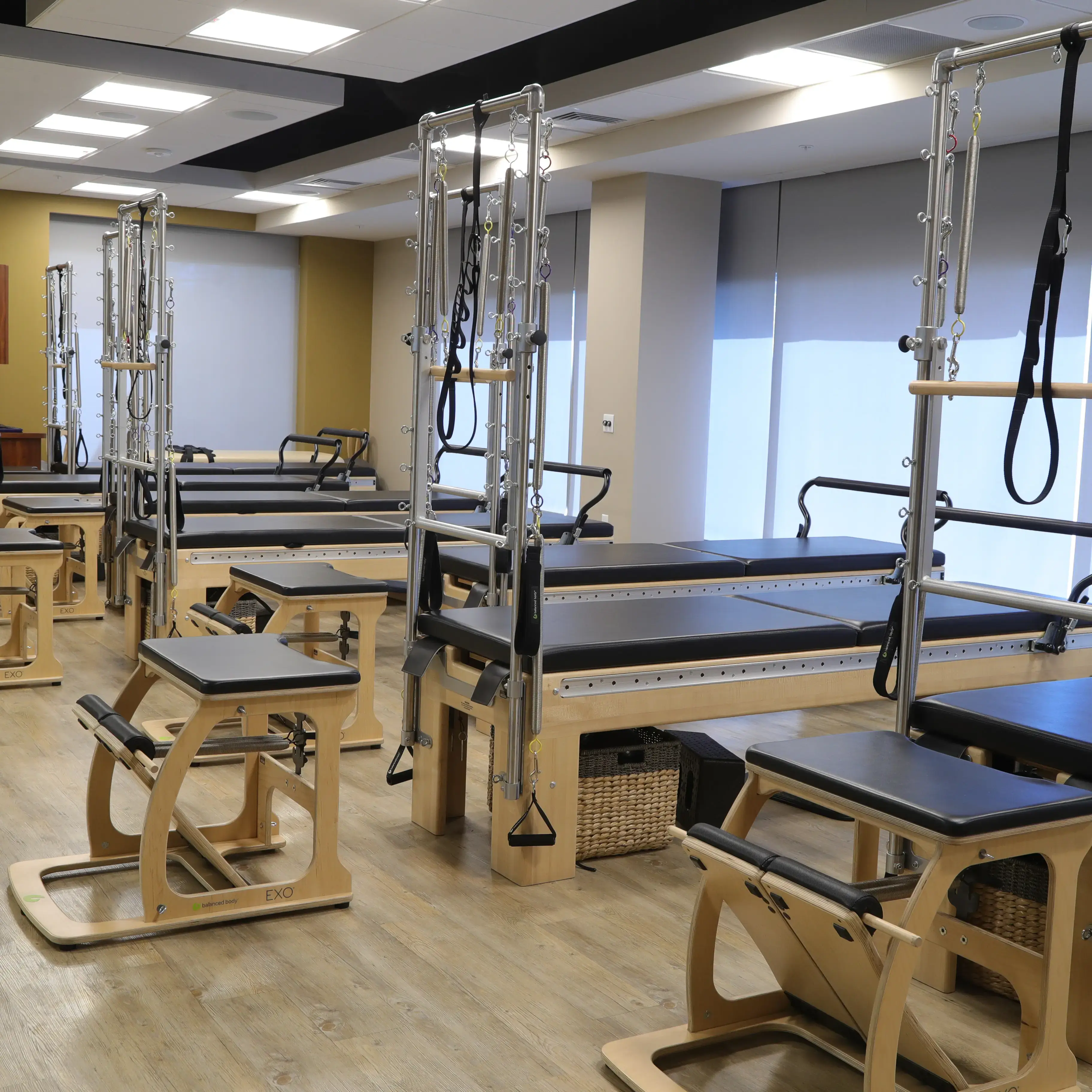 Village Clubs Camelback Pilates studio with wooden reformers, bright lighting, large windows, and organized storage baskets.