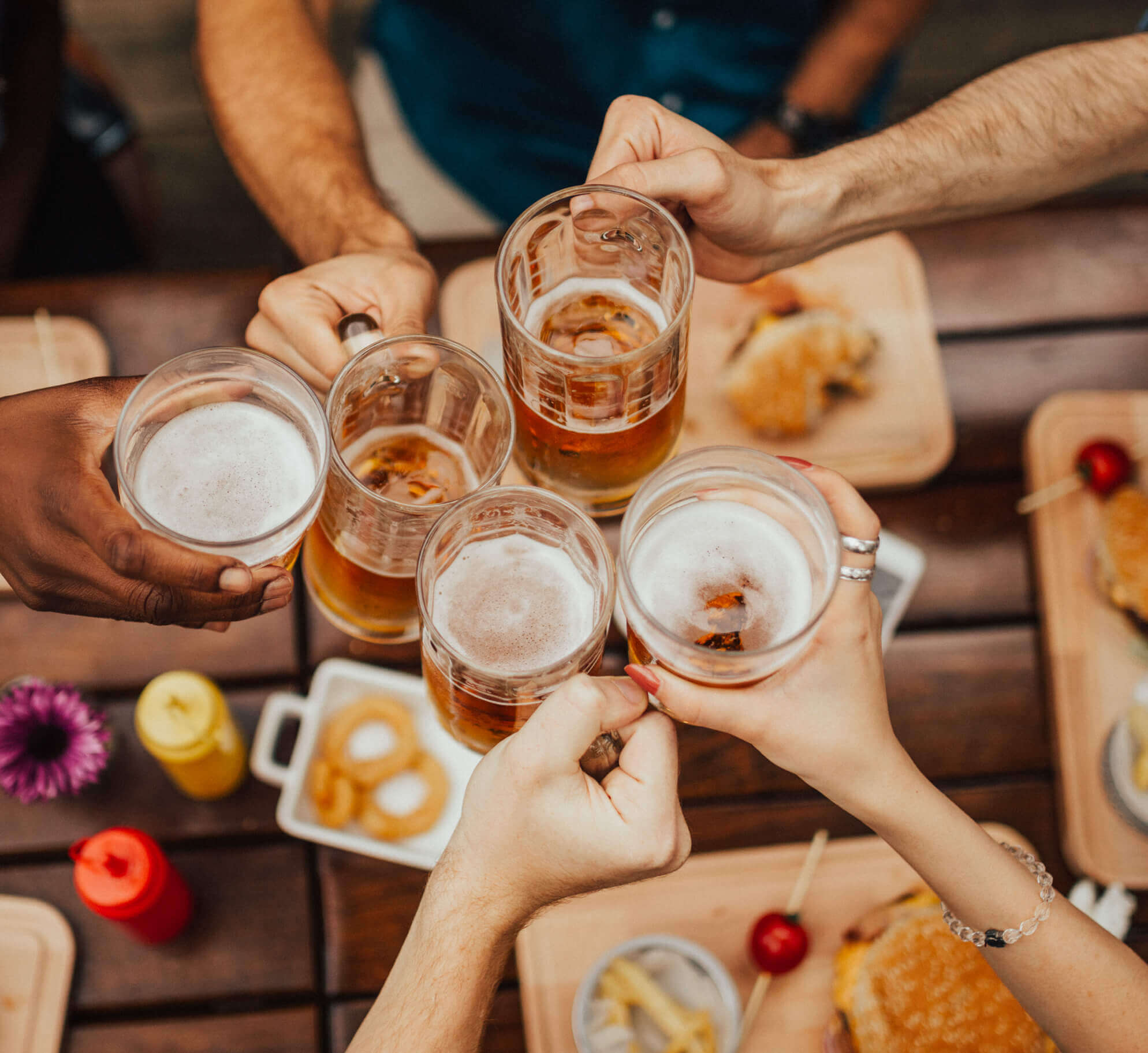 Guests toast with beer mugs over burgers and fries at Village Clubs Camelback, enjoying a relaxed outdoor dining experience.