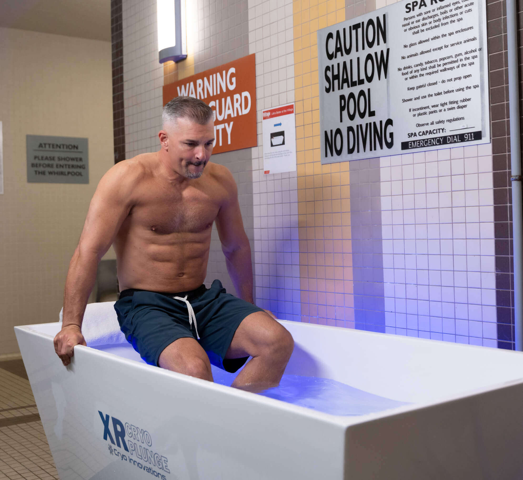 At Village Clubs Camelback, a man prepares for recovery by entering an ice bath in the pool facility, safety signs visible nearby.