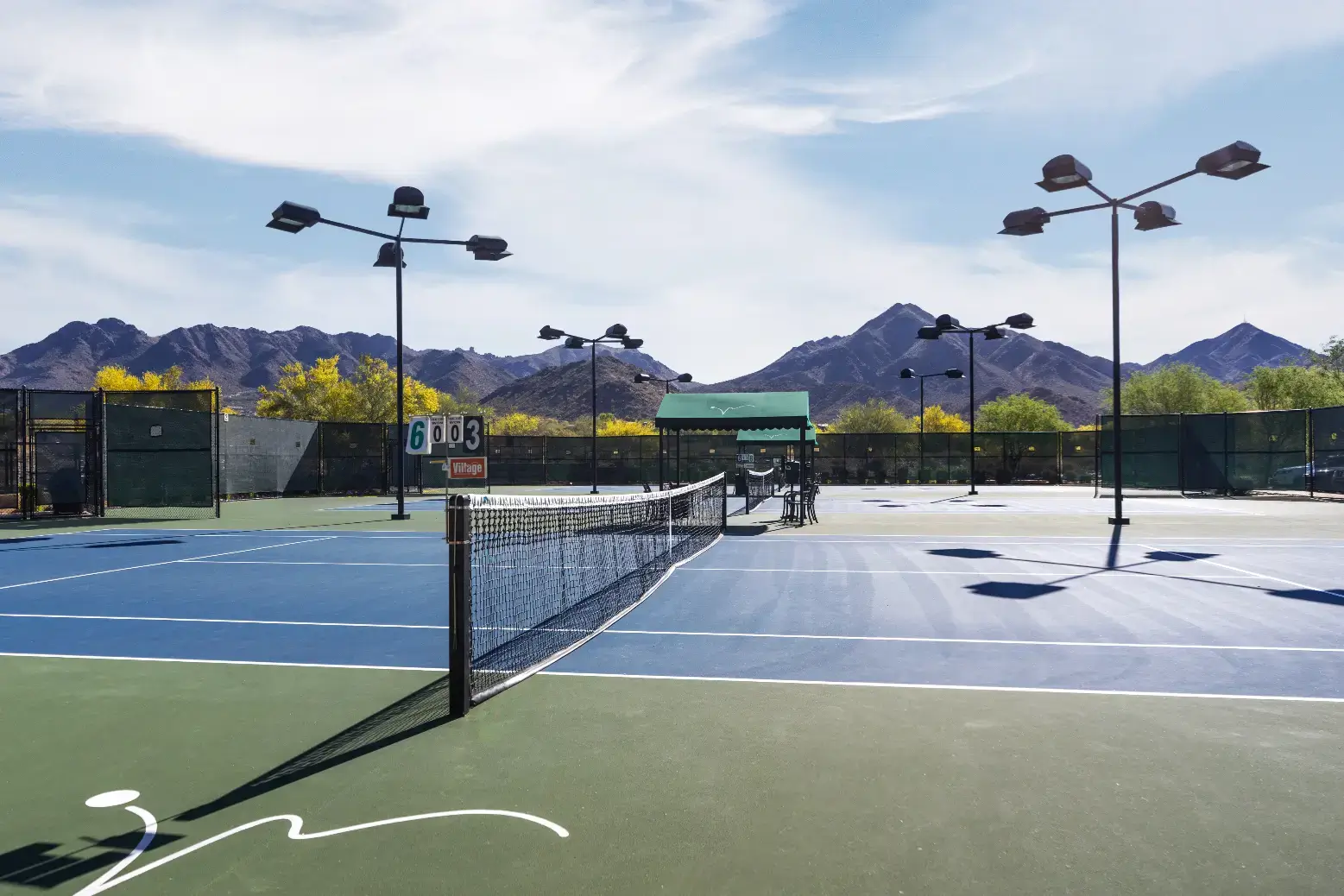 Village Clubs Camelback outdoor tennis courts with blue-green surfaces, mountain views, fencing, benches, and scorekeeper.