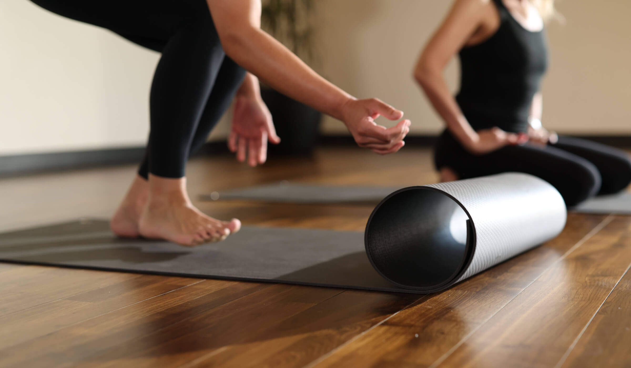 At Village Clubs Camelback, two members in black athletic wear prepare for yoga on mats atop a polished wood studio floor.